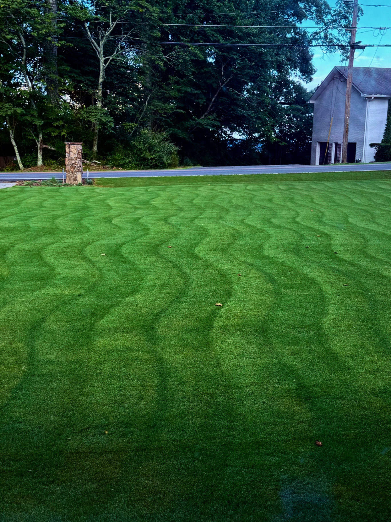Freshly mowed lawn with bold striping, a stone mailbox post, and a quiet neighborhood road