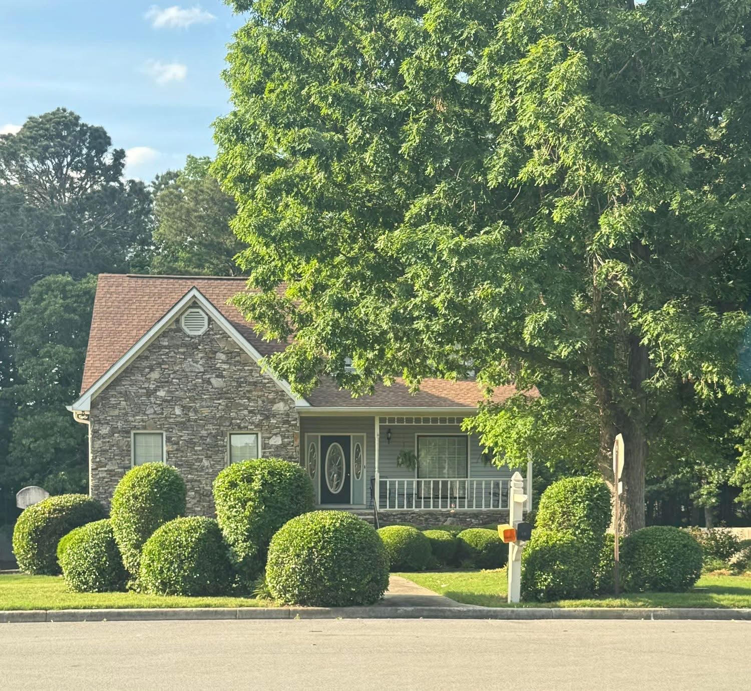 Stone-front home with neatly shaped round shrubs and a tidy lawn